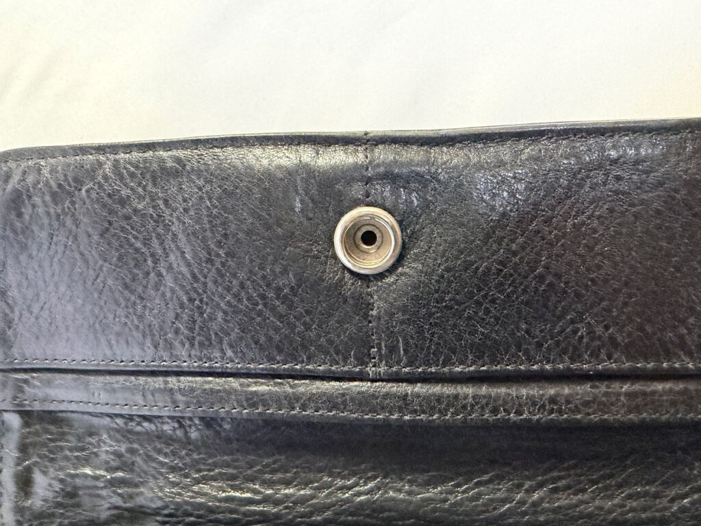 ジュディウォレットのクロスボタンは構造が複雑なため、今回はボタンパーツを外さず、財布全体を保護して固定した上で作業しました。
ドリルで下穴を空け、タンザナイトと同じ直径で石合わせを行い、最後にタガネで爪を起こして石留めしています。
「財布の雰囲気を変えずにワンポイントで色石を入れたい」方におすすめのカスタムです。